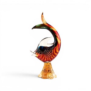 Könnte beinhalten: Eine farbenfrohe Glasfischskulptur mit gebogenem Schwanz und strukturierter Basis. Der Fisch hat Rot-, Orange-, Gelb- und Grüntöne. Die Skulptur ist ein dekoratives Element, wahrscheinlich für ein Zuhause oder Büro.