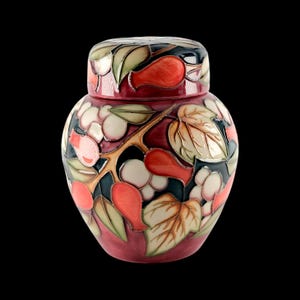 May include: A ceramic ginger jar with a lid, featuring a raised relief pattern of red pears, cream-coloured berries, and green leaves against a dark background. The surface has a glossy finish with distinct outlines separating the colourful motifs.