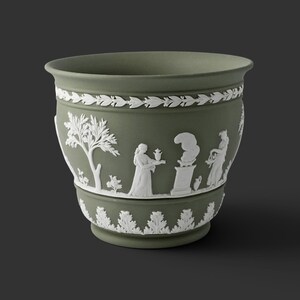 May include: A sage green ceramic planter featuring white relief ornamentation. The exterior displays a band of laurel leaves at the top and bottom, with a central frieze depicting classical figures, a tree, and an altar with smoke.