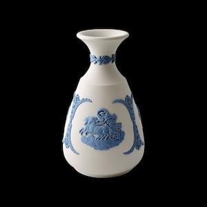 Może przedstawiać: Biały ceramiczny wazon z niebieskimi wzorami w płaskorzeźbie. Wazon przedstawia klasyczną scenę postaci w rydwanie ciągniętym przez konie, otoczoną dekoracyjnymi niebieskimi obramowaniami i wieńcem laurowym wokół szyi. Wazon ma pękaty korpus i rozszerzoną krawędź.