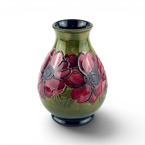 May include: A green ceramic vase with a dark blue rim and base. The vase features a floral design with red and pink flowers with blue centres. The flowers are set against a green background.
