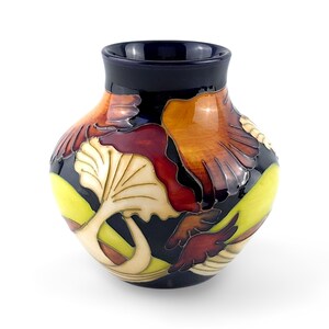 May include: A ceramic vase with a dark blue base color featuring a raised, multi-colored floral pattern in shades of cream, yellow, orange, and deep red. The vase has a rounded body, a narrow neck, and a smooth, glossy finish throughout the surface.