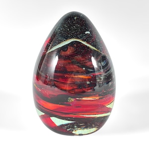 Könnte beinhalten: Ein rotes, schwarzes und weißes Glaseier mit wirbelnden Mustern. Das Ei ist glatt und glänzend.