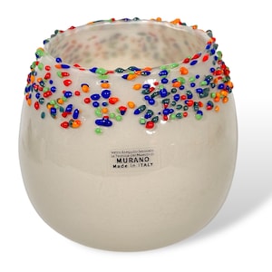 Puede incluir: Un portavelas de vidrio blanco con un borde decorativo de cuentas de vidrio de colores. El portavelas tiene una etiqueta que dice "Vetro Squisito Secco, La Tecnica dei Maestri di Murano, Made in Italy."