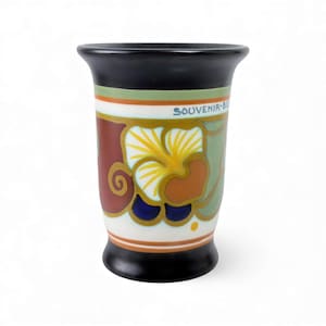 Op de afbeelding: Een keramische vaas met een zwarte rand en voet, met een bloemenontwerp in geel, bruin en groen. De vaas heeft de tekst "SOUVENIR-BE" in blauw. Het ontwerp bevat gouden accenten en een witte achtergrond.