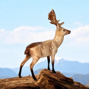 May include: A porcelain figurine of a brown and white deer with antlers standing on a wooden log. The deer is facing to the right and has a spotted pattern.