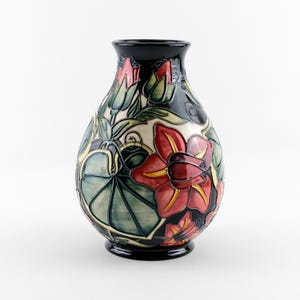 May include: A ceramic vase with a bulbous shape and a glossy black rim and base. The surface features a raised relief design of large red flowers, green leaves, and smaller buds against a cream-coloured background with black outlines.