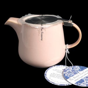 May include: A pale pink ceramic teapot with a stainless steel infuser and handle. The teapot has a curved spout and a rounded body. The handle is a lighter shade of pink. The teapot has a capacity of 600ml. The British Tea Company label is attached.