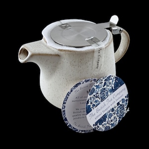 May include: A 600ml speckled off-white ceramic teapot with a stainless steel lid and infuser. The teapot features a side handle and a spout. Attached are two circular paper tags with blue floral patterns and text reading The British Tea Company.