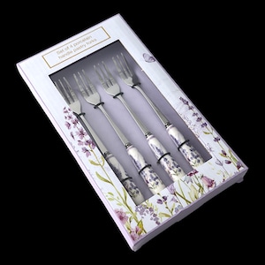 Op de afbeelding: Een set van vier gebaksvorken in een decoratieve doos. De vorken hebben roestvrijstalen tanden en handvatten met een lavendel bloemenpatroon. De doos is wit met lavendel bloemaccenten en de tekst "Set of 4 porcelain handle pastry forks".