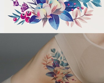 May include: A watercolor floral tattoo design featuring a large white flower with pink and blue accents, surrounded by smaller purple flowers and green leaves. The design also includes small red berries.