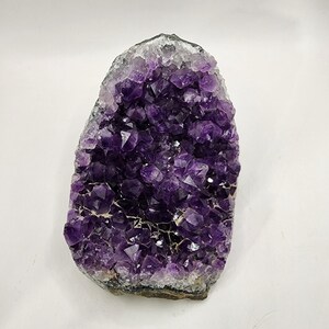 May include: A large amethyst crystal cluster with a purple and white color. The crystal is raw and has a natural shape.