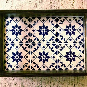 May include: A rectangular decorative tray with a dark wooden frame. The tray's interior features a tiled design with a white background and a repeating pattern of blue floral and geometric shapes.