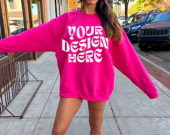 Puede incluir: Una sudadera rosa brillante con el texto "YOUR DESIGN HERE" en letras blancas. La sudadera es de gran tamaño y tiene cuello redondo.
