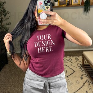 Può includere: Una maglietta a maniche corte color bordeaux con la scritta "YOUR DESIGN HERE" stampata in bianco sul davanti.