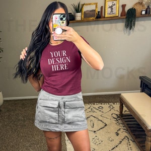 Può includere: Una maglietta corta color granata con il testo "YOUR DESIGN HERE" in bianco. La maglietta è indossata da una persona con capelli lunghi e neri e una gonna cargo grigia.