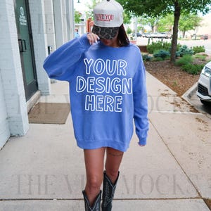 May include: A blue sweatshirt with the text "YOUR DESIGN HERE" in white. The person is wearing a baseball cap with the text "LOVE YOU" and black cowboy boots.