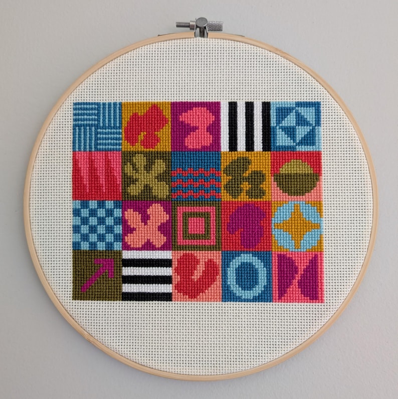 Puede incluir: Un dise&ntilde;o de punto de cruz geom&eacute;trico colorido en un aro de bordado de madera. El dise&ntilde;o presenta una variedad de formas y colores, incluyendo rosa, azul, verde, amarillo y negro.