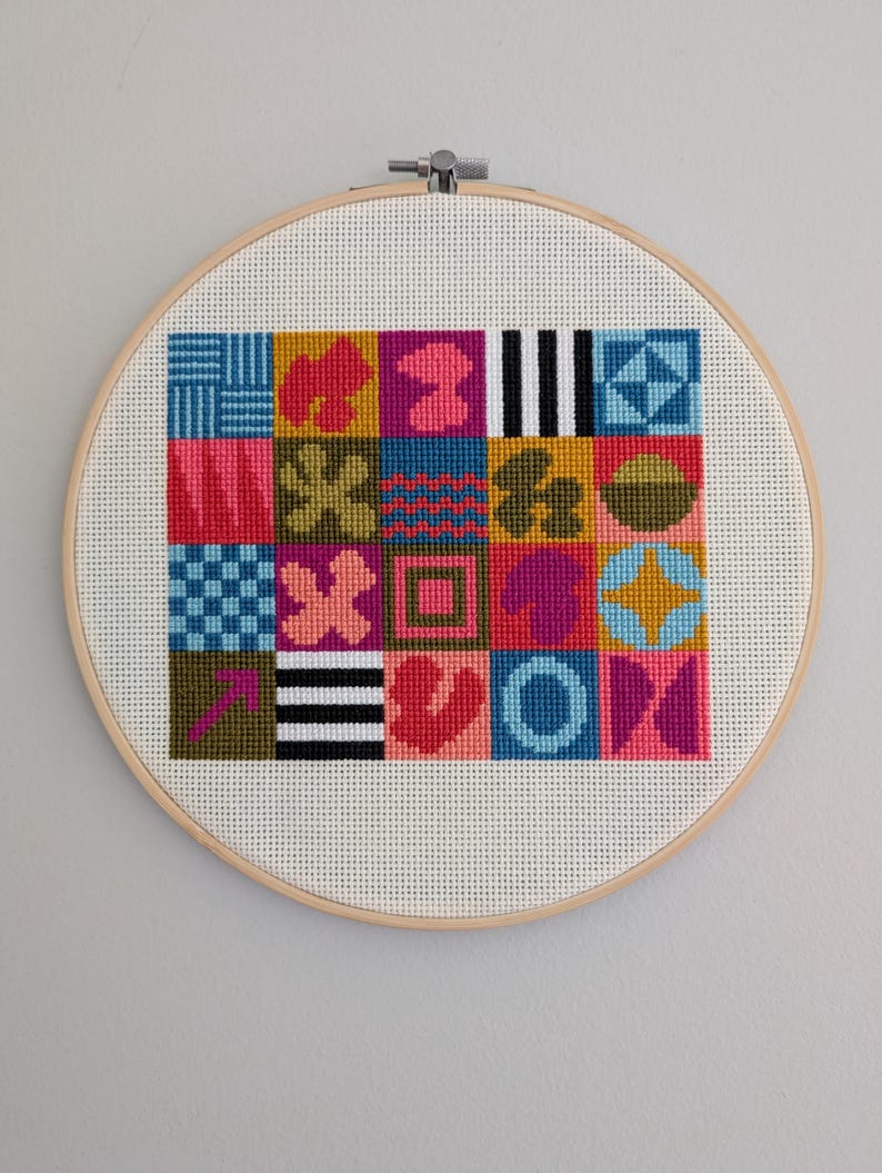 Puede incluir: Un dise&ntilde;o de punto de cruz geom&eacute;trico de colores en un aro de bordado de madera. El dise&ntilde;o presenta una variedad de formas y colores, incluyendo rosa, azul, verde, amarillo y blanco.