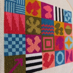 Puede incluir: Un aro de bordado de punto de cruz colorido con un patr&oacute;n geom&eacute;trico de cuadrados y varias formas en tonos de rosa, rojo, azul, verde, amarillo y blanco.