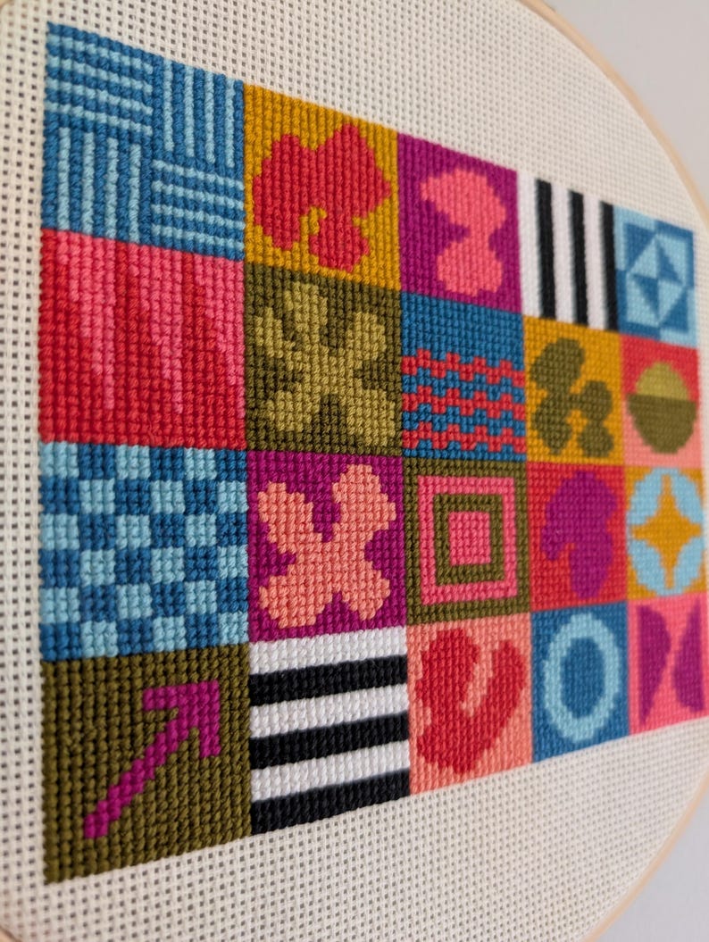 Puede incluir: Un aro de bordado de punto de cruz colorido con un patr&oacute;n geom&eacute;trico de cuadrados y varias formas en tonos de rosa, rojo, azul, verde, amarillo y blanco.