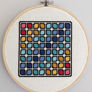 Puede incluir: Un aro de bordado de punto de cruz con un patrón geométrico colorido. El patrón está formado por pequeños cuadrados en tonos de azul, turquesa, amarillo y rojo. Los cuadrados están dispuestos en una cuadrícula, creando un efecto de degradado.