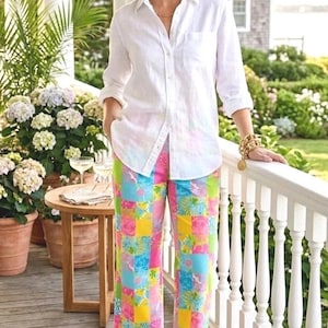 Puede incluir: Una persona con una camisa blanca y pantalones estampados coloridos. Los pantalones tienen un dise&ntilde;o de patchwork con cuadrados rosas, azules, amarillos y verdes. Lleva sandalias marrones y una pulsera dorada.
