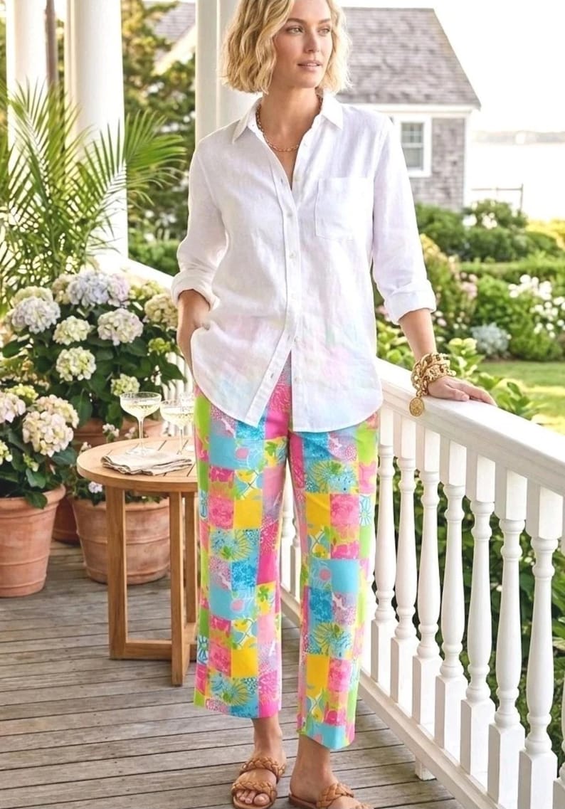 Puede incluir: Una persona con una camisa blanca y pantalones estampados coloridos. Los pantalones tienen un dise&ntilde;o de patchwork con cuadrados rosas, azules, amarillos y verdes. Lleva sandalias marrones y una pulsera dorada.