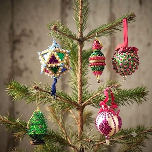 May include: Five decorative ornaments hanging on a pine tree branch. One is a multi-faceted geometric shape with blue, green, and purple panels. Others include a green and pink beaded teardrop, a green ball with pink flowers, a green cone, and a white ball with pink sequins.