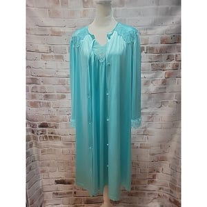 May include: A vintage light blue satin robe and nightgown set. The robe features long sleeves, a button-down front, and delicate lace trim on the sleeves and neckline. The nightgown is visible underneath, with a matching lace detail. The set is displayed on a mannequin.