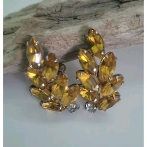 May include: Vintage clip-on earrings with a leaf design. Each earring features amber-coloured, marquise-cut rhinestones set in gold-tone metal. Small, clear rhinestones are at the base of each earring, adding sparkle.