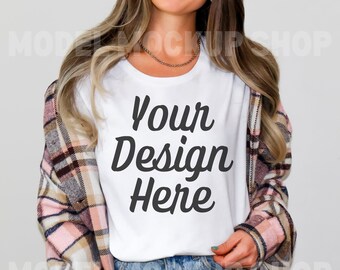 Puede incluir: Una camiseta blanca con el texto "Your Design Here" en escritura cursiva negra. La camiseta la lleva puesta una persona con el pelo largo y castaño y una camisa de cuadros. La persona lleva unos vaqueros azules.