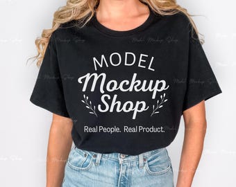 May include: Black t-shirt with the text "MODEL Mockup Shop" in white script. The shirt also has the text "Real People. Real Product." in a smaller font. The model is wearing light blue jeans.