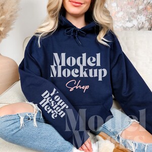 Op de afbeelding: Een marineblauwe hoodie met de tekst "Model Mockup Shop" in wit en "Your Design Here" in wit op de mouw.