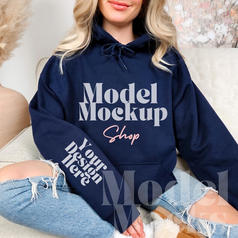 Op de afbeelding: Een marineblauwe hoodie met de tekst "Model Mockup Shop" in wit en "Your Design Here" in wit op de mouw.