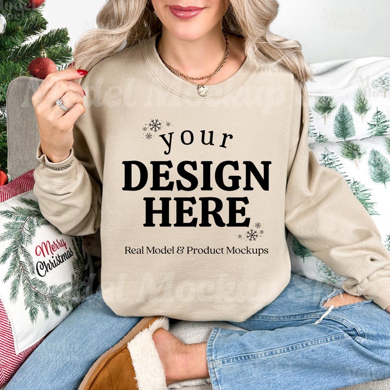 May include: A tan sweatshirt with the text "your DESIGN HERE" in black, with snowflake accents. The words "Real Model & Product Mockups" are below the main text. The model is wearing blue jeans and brown slippers.