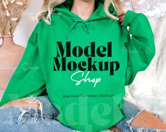 May include: A green hooded sweatshirt with the text "Model Mockup Shop" in black lettering. The text "Real Model & Product Mockups" is printed in white below the main text.