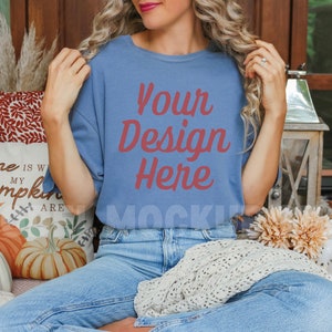 May include: A woman wearing a blue t-shirt with the text "Your Design Here" in red. She is sitting on a couch with a white pillow that says "Home is where my pumpkins are".
