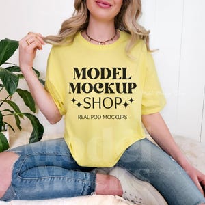 Könnte beinhalten: Ein gelbes T-Shirt mit dem Text "MODEL MOCKUP SHOP" und "REAL POD MOCKUPS" darauf gedruckt. Das Model trägt eine blaue Jeans und weiße Sneaker.