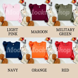May include: A collection of six crewneck sweatshirts in various colors: light pink, maroon, military green, navy, orange, and red. Each sweatshirt is displayed with a label indicating its color. The sweatshirts are arranged on a neutral background.