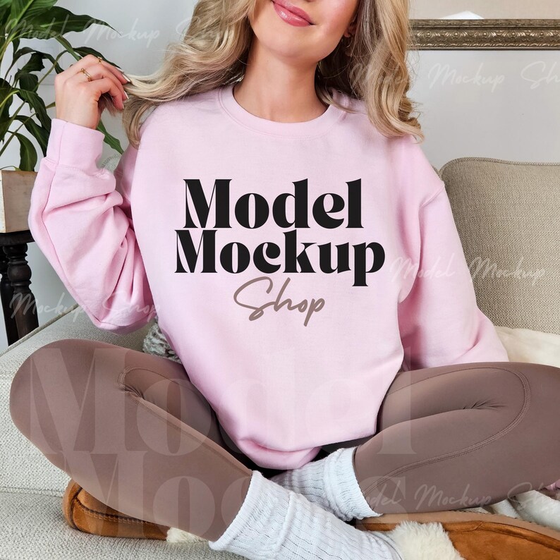 Peut inclure: Un sweat-shirt rose avec le texte "Model Mockup Shop" en lettres noires et brunes.