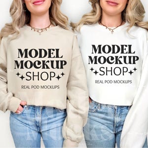 Op de afbeelding: Twee vrouwen dragen crème en witte sweatshirts met de tekst "MODEL MOCKUP SHOP" en "REAL POD MOCKUPS" erop gedrukt. Beide vrouwen dragen een blauwe jeans.