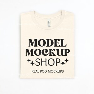May include: A beige t-shirt with the text "MODEL MOCKUP SHOP" and "REAL POD MOCKUPS" printed on it.