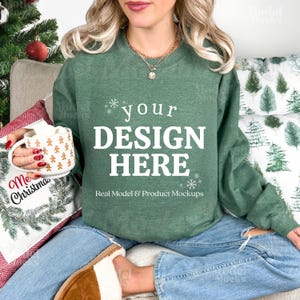 May include: A green sweatshirt with the text "your DESIGN HERE" in white. The sweatshirt is part of a product mockup, with a Christmas theme. A mug with gingerbread men and a pillow with a Christmas design are also visible.