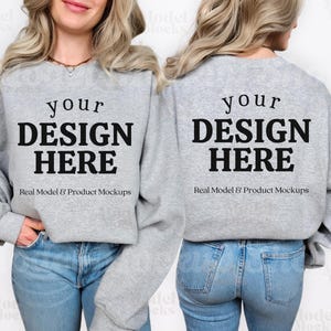 May include: A heather gray sweatshirt with the text "your DESIGN HERE" in bold black letters. Below the text is the text "Real Model & Product Mockups" in a smaller font. The sweatshirt is being worn with blue jeans.