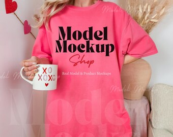 May include: A vibrant pink t-shirt with the text "Model Mockup Shop" in black and red. A white mug with "XO XOXO" and a heart is held in the hand. The image has a Valentine's Day theme.