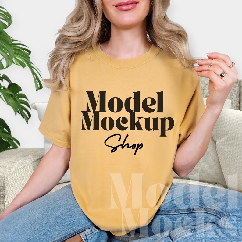 May include: Mustard yellow t-shirt with the text "Model Mockup Shop" in black. The shirt is a crew neck and appears to be made of a soft material. The model is wearing blue jeans.
