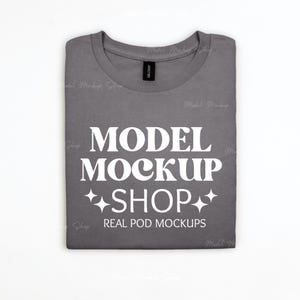 May include: A folded gray t-shirt with the text "MODEL MOCKUP SHOP REAL POD MOCKUPS" in white. The shirt has a crew neck and a black tag. The shirt is on a white background.