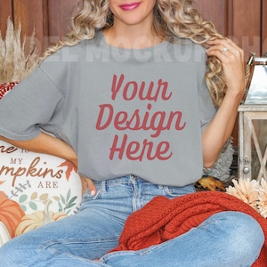 May include: A woman wearing a gray t-shirt with the text "Your Design Here" in red. She is sitting on a couch with a pillow that says "Home is my pumpkins are".