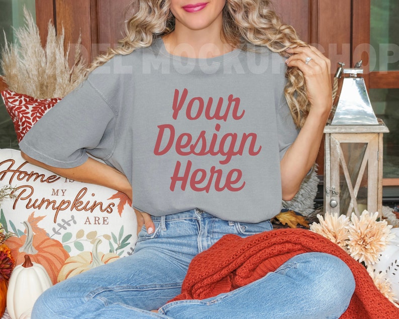 May include: A woman wearing a gray t-shirt with the text "Your Design Here" in red. She is sitting on a couch with a pillow that says "Home is my pumpkins are".